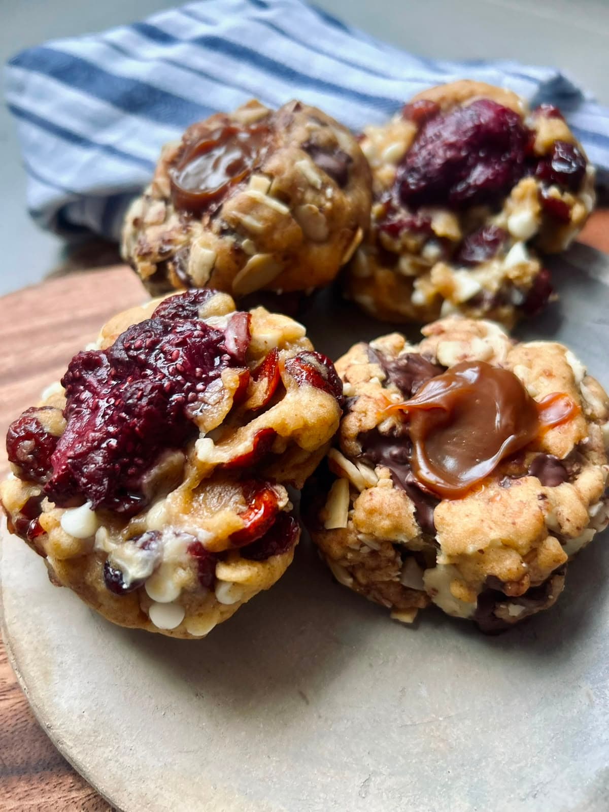 Cuatro galletas NY Cookies sobre un plato de cerámica: dos coronadas con salsa de frutos rojos y arándanos, y dos con arequipe derretido entre trozos de chocolate y almendras.